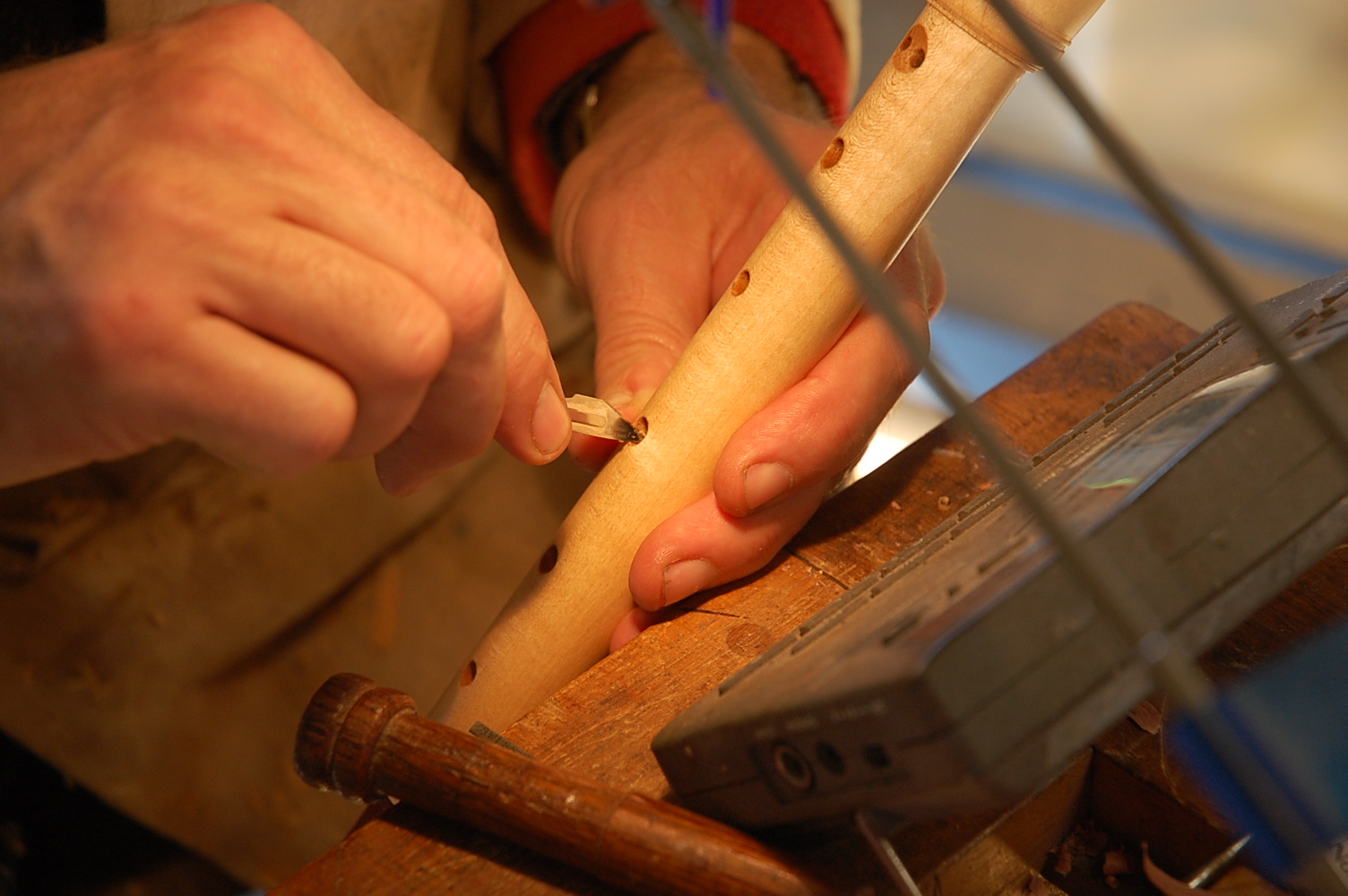 Tim carefully inserts a scalpel blade into a finger hole, and scrapes away wood.